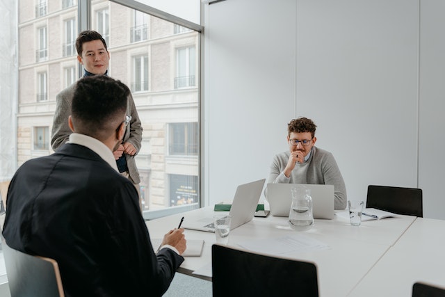 three people in a conference room looking at their computers and talking